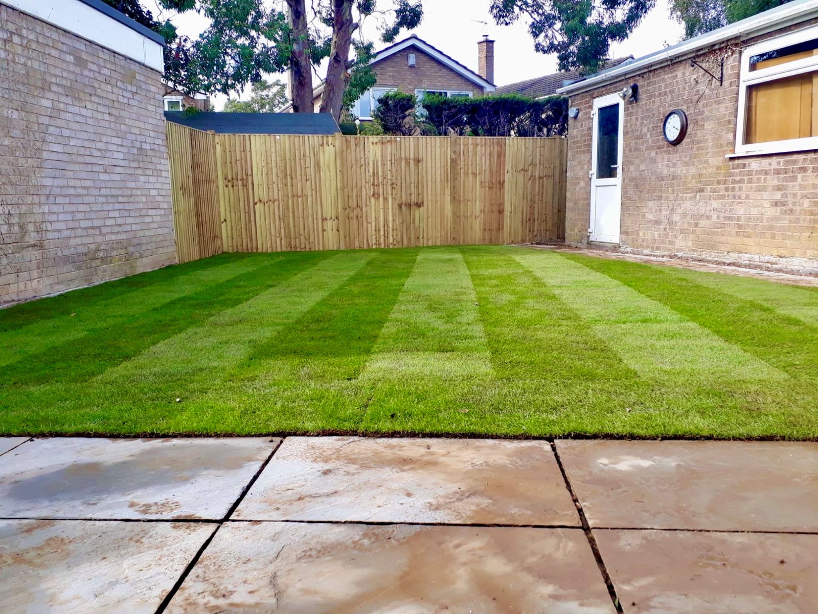 Striped turf lawn laid up to a new fence and patio