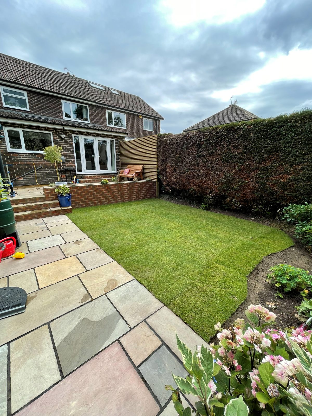 New lawn laid beside sandstone paving and a clipped hedge