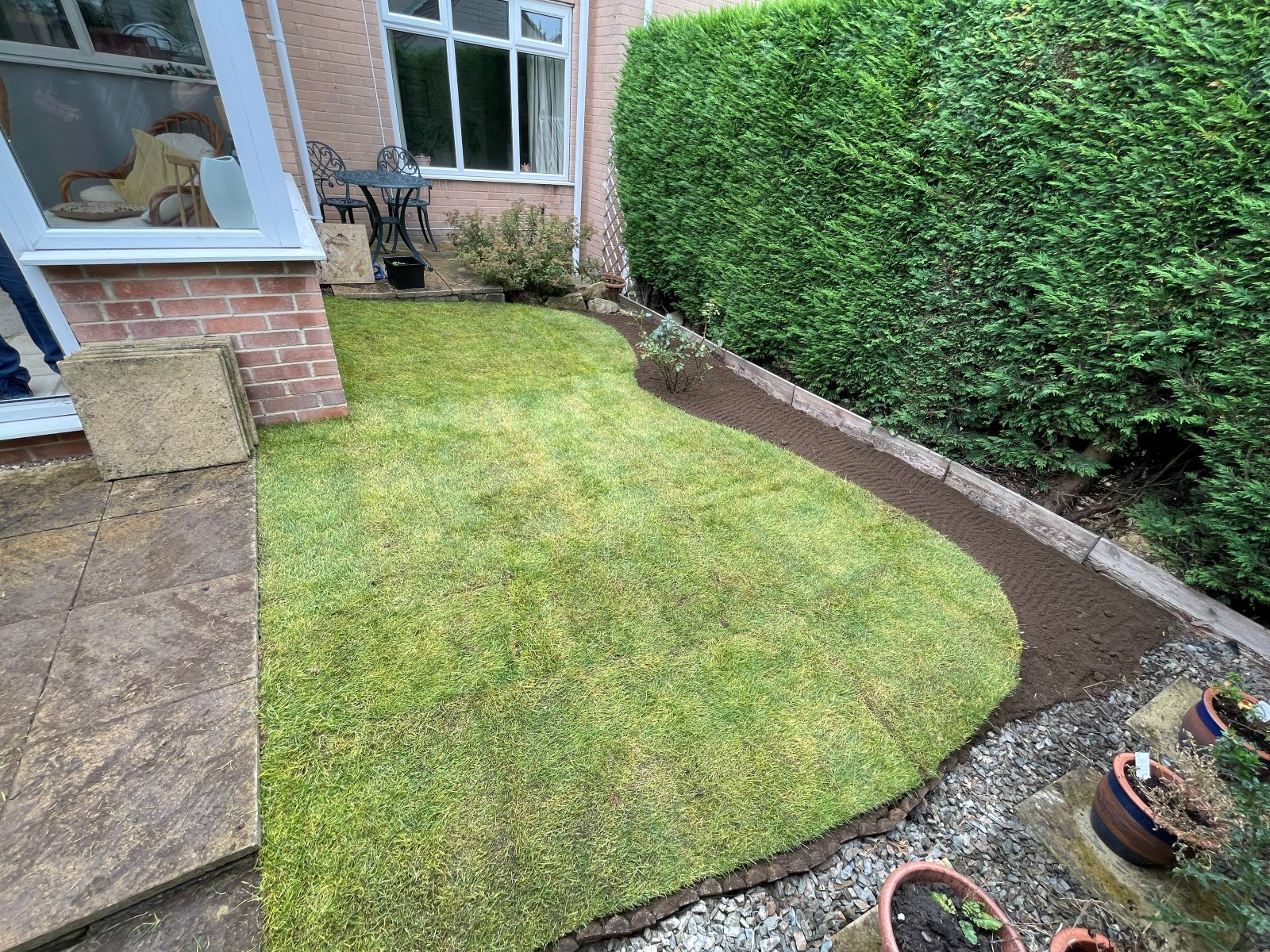 Freshly laid lawn with a curved edge next to a conifer hedge
