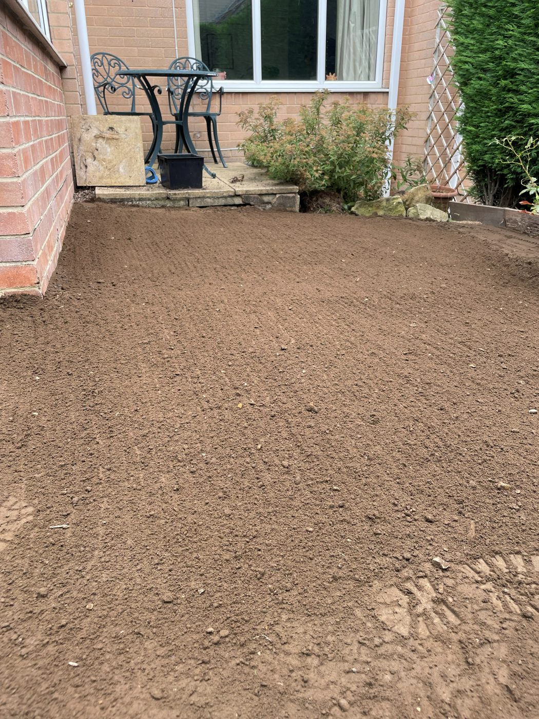 Soil raked and graded to a level seedbed, falling away from the house, ready for turf